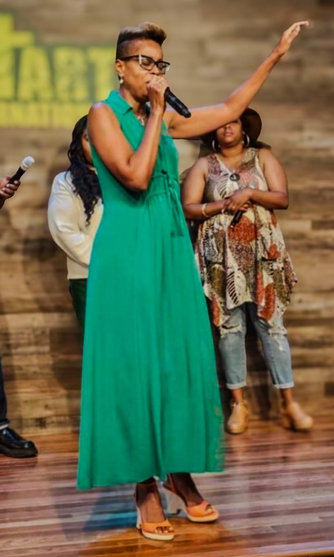 A woman sings into a microphone with her hand raised in worship