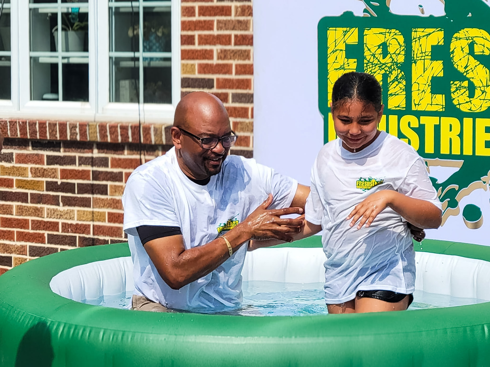 A baptism takes place outdoors in a pool in front of the church